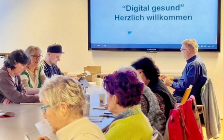 Teilnehmerinnen und Teilnehmer beim Workshop „Digital gesund – KI im Gesundheitsalltag“ von WIGA Digital in Marchtrenk. Die Gruppe sitzt gemeinsam an einem Tisch und verfolgt die Präsentation auf einem großen Bildschirm. Der Workshop zeigt, wie künstliche Intelligenz dabei helfen kann, medizinische Befunde und Gesundheitsinformationen besser zu verstehen.